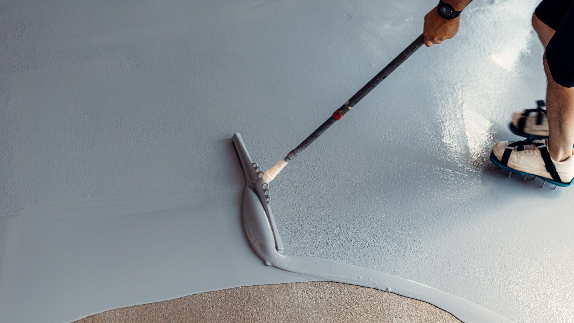A construction worker apply grey epoxy resin in an industrial hall