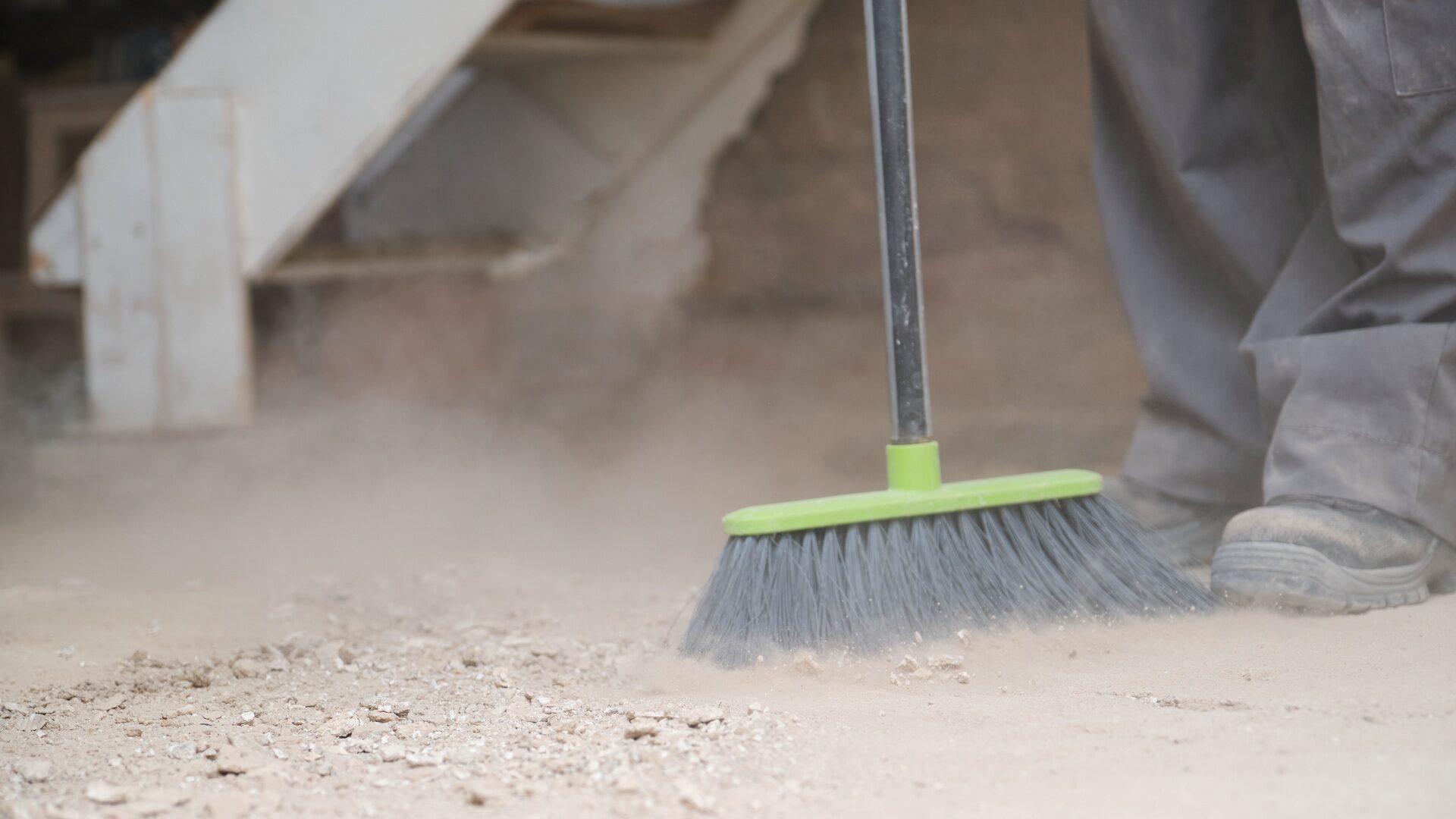 Unrecognizable young builder sweeping the floor at a construction site.